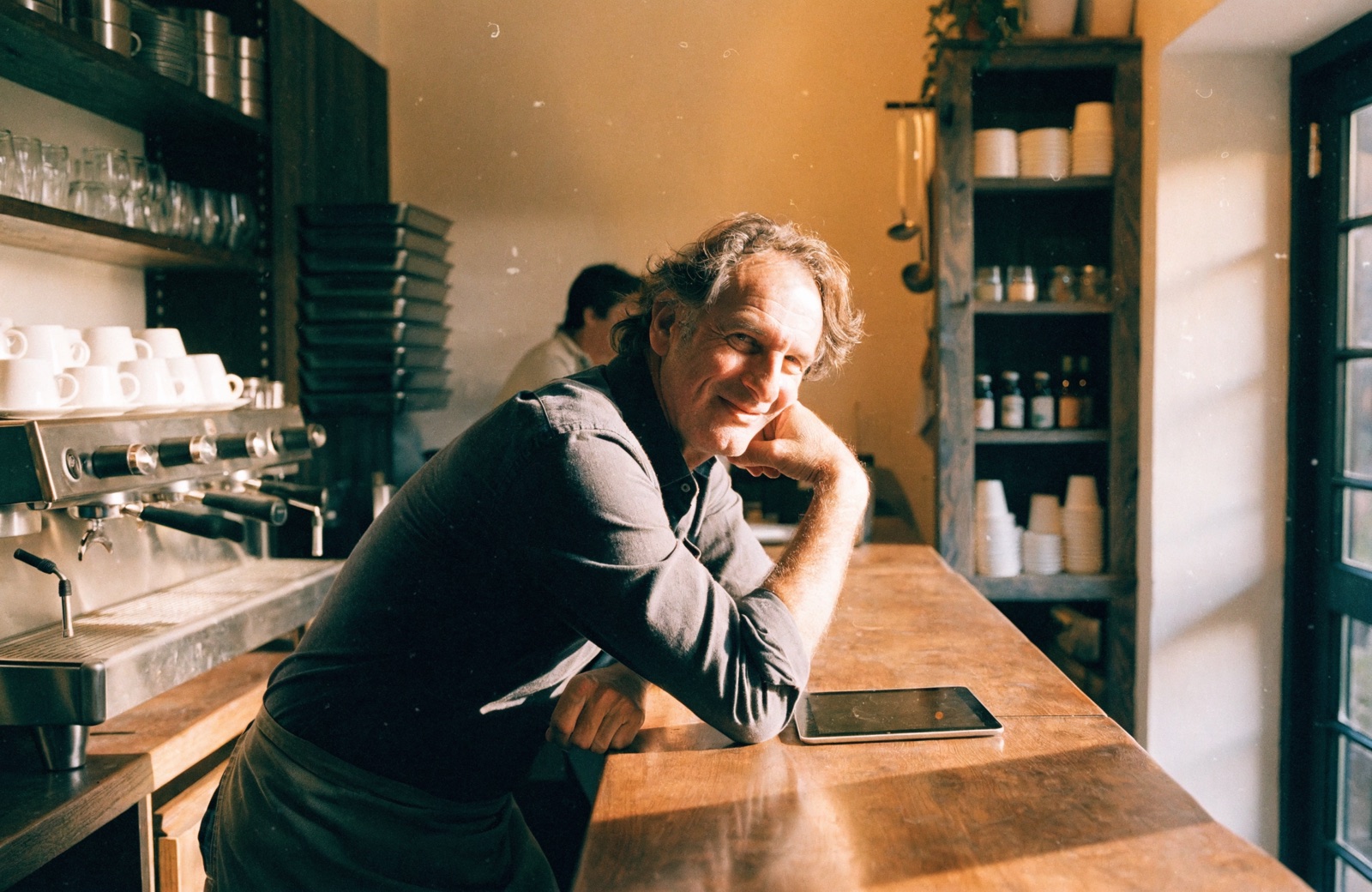 A cafe owner leaning on the counter with a tablet in the quiet after the lunch rush