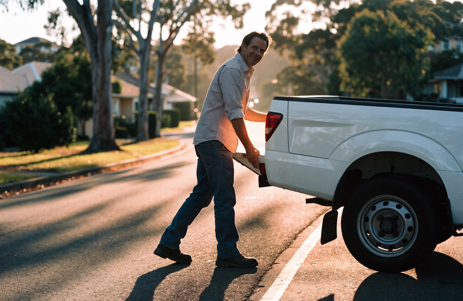 A tradesperson closing the tailgate of his ute in golden late-afternoon light, finished for the day