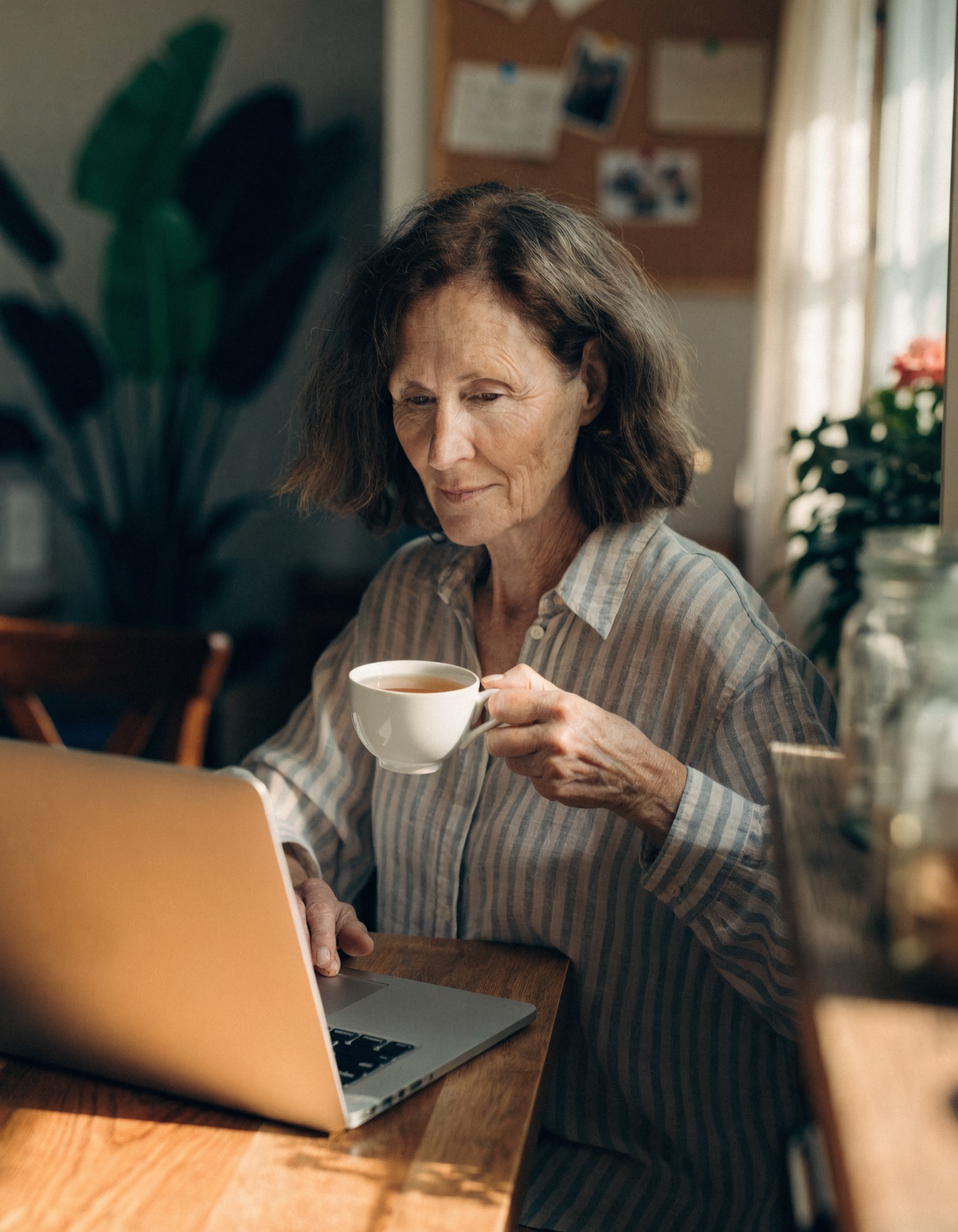 A business owner at her kitchen table with a cup of tea, calmly checking one page on a laptop